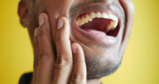A man suffers from a severe toothache. He holds his cheek with his hand. If you have a toothache, always visit a dentist, e.g. Dr. med Cornelia Katumba at the Zahnlounge in Zurich-Enge.