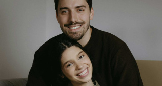 Ein sitzendes Paar. Beide lächeln. Veneers können helfen ein natürliches Lächeln wieder herzustellen, wenn etwa Zahnfehlstellungen, kleine Schäden und Verfärbungen das ästhetische Erscheinungsbild des Gebisses beeinträchtigt haben.