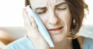 A woman suffers from a toothache. She holds a cold pack on her left cheek to cool the affected area. A visit to the dentist is strongly recommended for toothache.